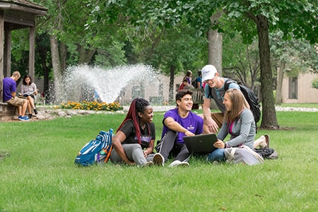 Diverse group of students sit together on a grassy lawn