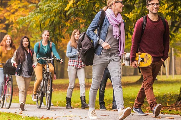 Group of students walk and bike across campus surrounded by colorful fall foliage 