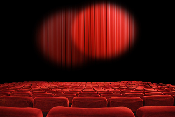 An empty theatre with spotlight on a red curtain and red cushion stadium style chairs