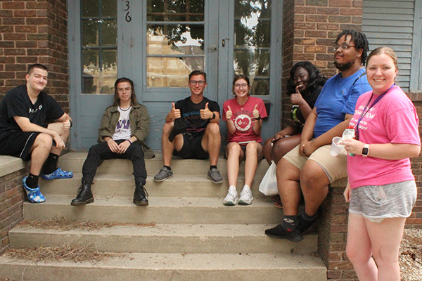 Diverse group of students siting on steps in front of a house.