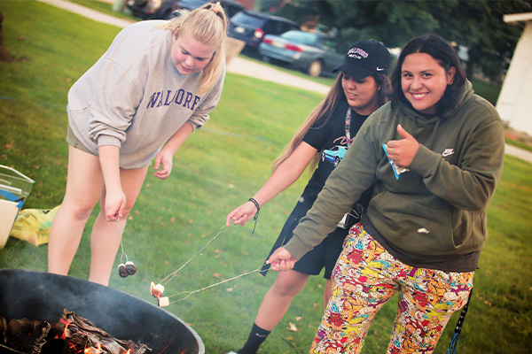 Three female students roasting marshmallows over a campfire